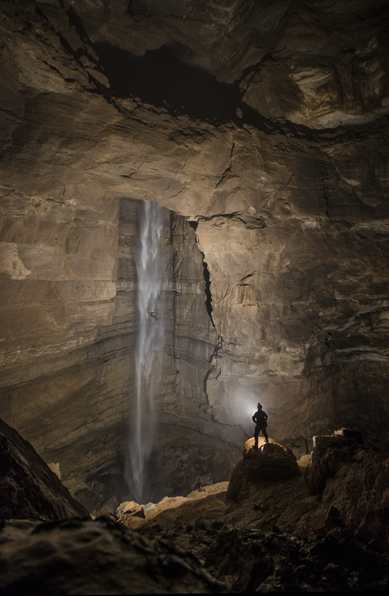 Caver standing in front of underground waterfall.